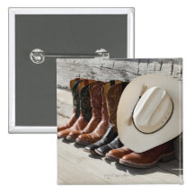 Cowboy hat on row of cowboy boots outside a log pinback button