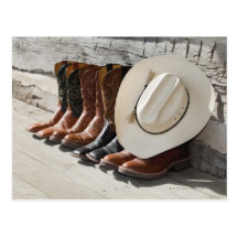 Cowboy hat on row of cowboy boots outside a log postcard