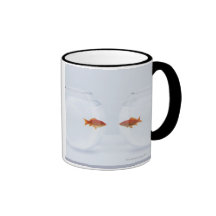 Goldfish in separate fishbowls looking face to coffee mugs