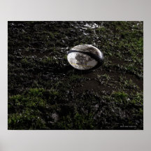 Muddy rugby ball sitting on a chewed up grass posters
