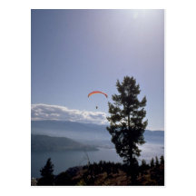 Paraglider flying over valley lake post card