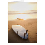 Surfboard laying on beach at sunset greeting cards