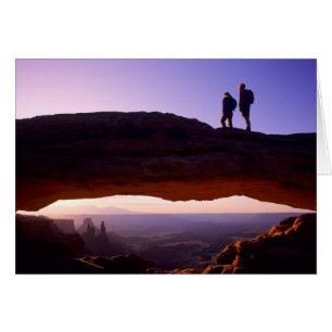 A couple watches sunrise from atop Mesa Arch in