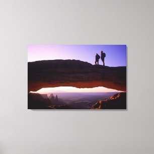 A couple watches sunrise from atop Mesa Arch in Canvas Print