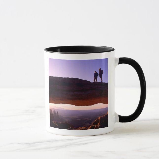 A couple watches sunrise from atop Mesa Arch in Mug (Right)