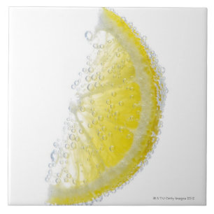 A juicy ripe organic lemon wedge fruit submerged tile
