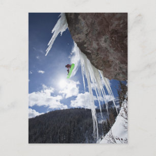 A male snowboarder jumps off an ice waterfall postcard