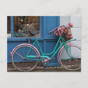 A pink bicycle with wicker basket and flowers postcard