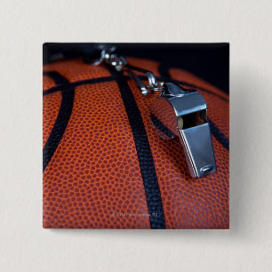 A referee's whistle rests on top of a 15 cm square badge