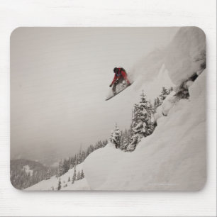 A snowboarder jumps off a cliff into powder in mouse mat