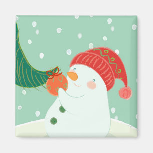 A snowman hanging an ornament on a tree magnet