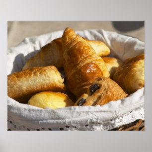 A wicker breakfast basket with croissants, and poster