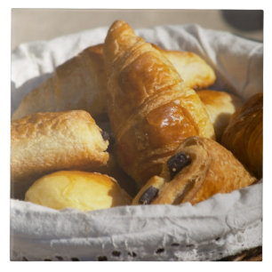A wicker breakfast basket with croissants, and tile