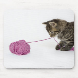 A young tabby kitten playing with a ball of mouse mat