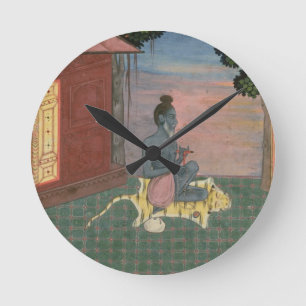 Aged ascetic seated on a tiger skin outside a buil round clock