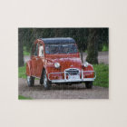 An old red Citroen 2CV car with a smiling woman