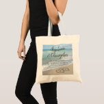 Beach Wedding Monogram Hearts in the Sand Tote Bag<br><div class="desc">Focus on the bride and groom names and initials in the beach sand, drawn inside a heart! Elegant Sand Hearts Beach Destination Wedding Matching set features Beautiful scenic landscape image of clear aqua turquoise ocean water, with white waves crashing on the sand beach.Hearts symbolise lasting love! Florida Beach Design and...</div>