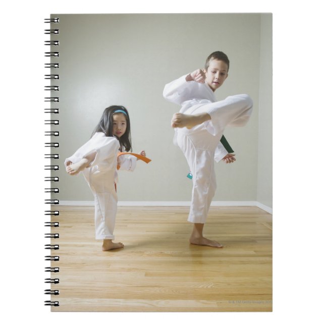 Boy and girl (4-9) practising Taekwondo kicks Notebook (Front)