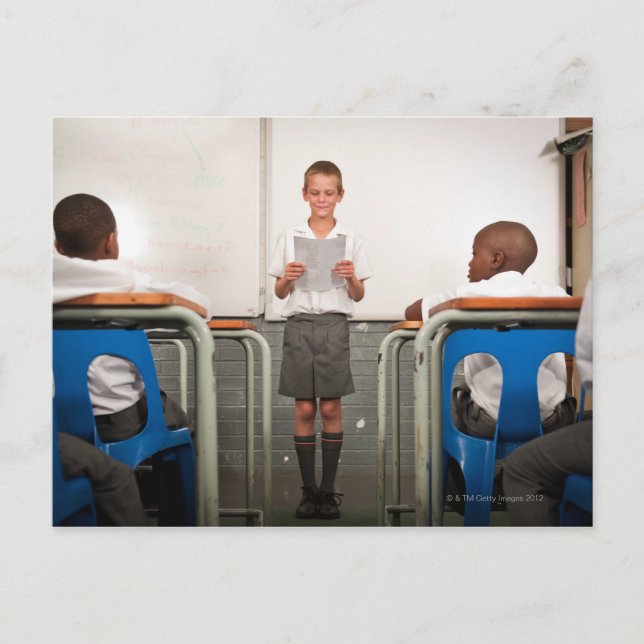 Boy standing in front of class reading in postcard (Front)