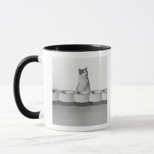 Cat sitting and licking beside pet bowl on white mug