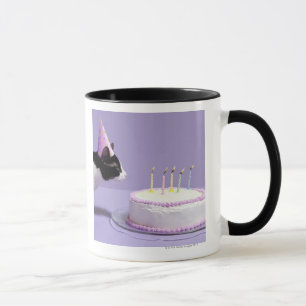 Cat wearing birthday hat blowing out candles on mug