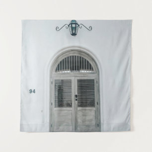 CLOSED GREY WOODEN DOOR BELOW BLACK LIGHT SCONCE TAPESTRY