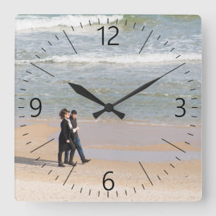 Couple walking along a shoreline square wall clock