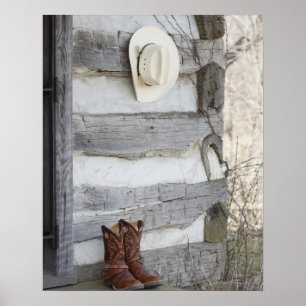 Cowboy boots and hat outside of log cabin poster