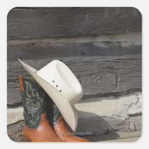 Cowboy hat on cowboy boots outside a log cabin square sticker