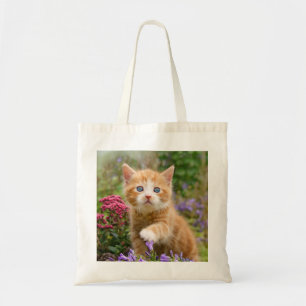 Cute ginger kitten in a garden playing with flower tote bag