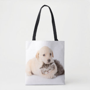 cute little cat sleeps in dog's hands tote bag