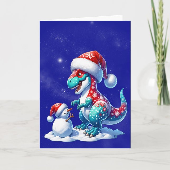 Dinosaur with santa hat building a snowman holiday card (Front)