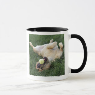 Dog laying upside down in grass with tennis ball mug