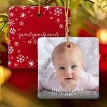 First Christmas Baby Photo Snowflakes Grandparents Ceramic Ornament<br><div class="desc">“First Christmas.” A playful visual of white snowflakes and handwritten script typography with customised year, overlaying the photo of your choice, help you usher in Christmas and New Year. On the back, additional white snowflakes and handwritten typography with “proud grandparents of baby’s name” overlay a red background. Feel the warmth...</div>