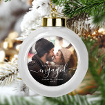 First Christmas Engaged Photo White Script Ceramic Ball Christmas Ornament<br><div class="desc">Commemorate your engagement with this beautiful modern keepsake ornament. The white text reads "Our first Christmas engaged, " with the word "engaged" in elegant handwriting script with flourishes before and after. Replace the sample image with your favourite photo, and add your names and the year. A dark gradient filter helps...</div>