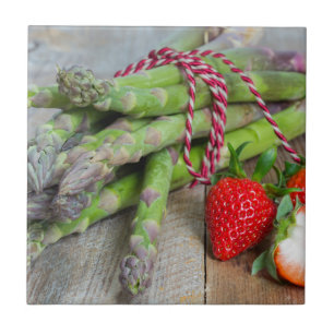 Green asparagus with strawberries on wooden tile