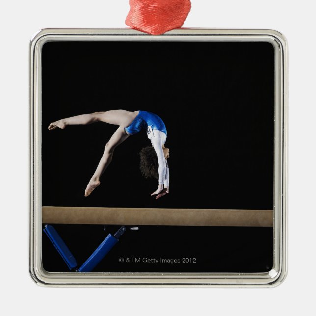 Gymnast (9-10) flipping on balance beam, side metal tree decoration (Front)