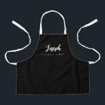 Little Chef Script Name personalised Black Apron<br><div class="desc">Make your little chef feel extra special with our Little Chef Script Name Personalised Kids black Apron. This apron is designed to provide a simple, chic, and elegant look, featuring stylish script typography for personalising the name. The purple background colour adds a touch of vibrancy and fun, perfect for engaging...</div>