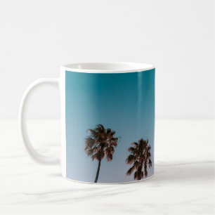 Low-angle photograph of three palm trees under blu coffee mug