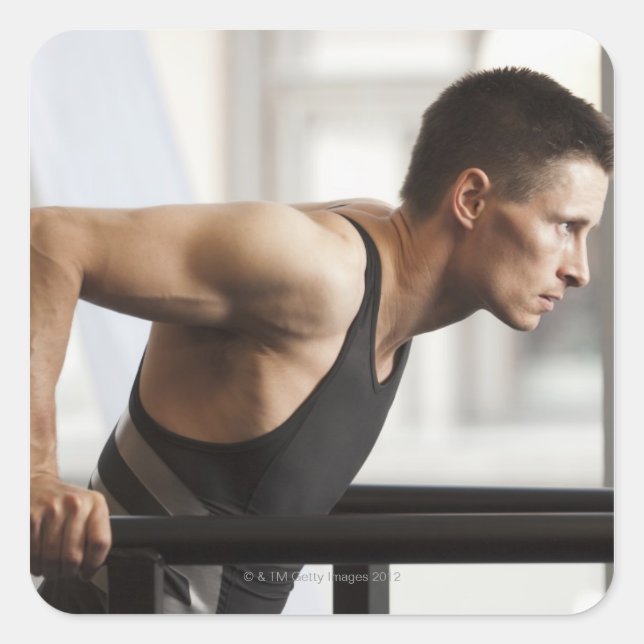Male athlete using gymnastics equipment in gym square sticker (Front)