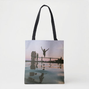Man jump in mid air on body of water tote bag