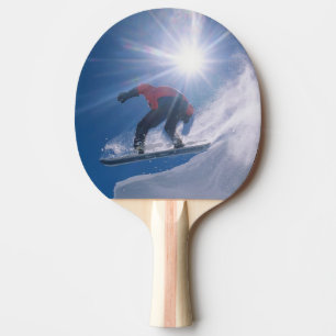 Man jumping off a large cornince on a snowboard ping pong paddle