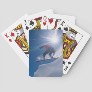 Man jumping off a large cornince on a snowboard playing cards