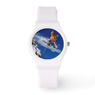 Man on a snowboard jumping off a cornice at watch