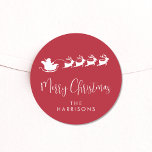 Merry Christmas Santa Reindeer Red Classic Round Sticker<br><div class="desc">Fun seasonal red sticker for your Christmas holiday cards and correspondence featuring a white silhouette of reindeers flying Santa's sleigh through air,  "Merry Christmas" in a stylish white script and your name in simple modern white typography.</div>