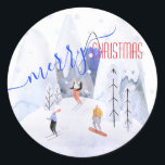 Merry Christmas Snowy Mountain Scene Skiers Classic Round Sticker<br><div class="desc">A quaint,  cute and happy Merry Christmas sticker painted in watercolors of skiers skiing on a mountain with snow and trees and a beautiful modern calligraphy saying Merry Christmas.</div>