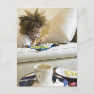 Mixed race boy reading book on sofa postcard