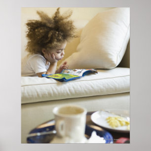 Mixed race boy reading book on sofa poster