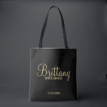 Modern Black and Gold Personalised Bridesmaids Tote Bag<br><div class="desc">Modern Black and Gold Personalised Bridesmaids Gifts featuring personalised bridesmaid's name in gold modern script font style with title and wedding date in modern sans serif font style on black background. Also perfect for Maid of Honour, Flower Girl, Mother of the Bride and more. Please Note: The foil details are...</div>