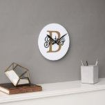 Modern Elegant Monogram Name  Black Gold Script  Round Clock<br><div class="desc">The Modern Elegant Monogram Name Black Gold Script Clock is a stylish and personalised timepiece perfect for any home or office setting. This clock features a sleek black face with elegant gold script, allowing you to customise it with your monogram and name. The modern design and sophisticated colour scheme make...</div>